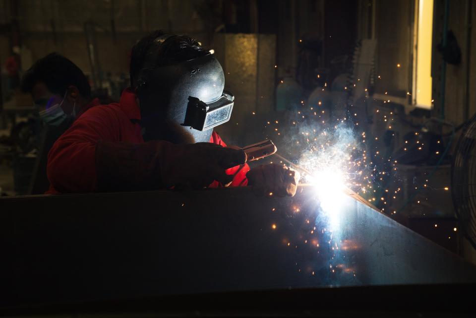 In this Monday, April 27, 2020 photo, a worker welds metal that will be a part of a gate system made by Guard ME that conducts temperature checks and fogs disinfectants on users, in Dubai, United Arab Emirates. As confirmed coronavirus cases spike, the United Arab Emirates is opening up its cavernous malls and restaurants in a gamble to stimulate its economy while still trying to fight off the pandemic. That's led to a new normal here of temperature checks, social distancing monitors at supermarkets and marked-off empty seats on the city's driverless Metro. (AP Photo/Jon Gambrell)