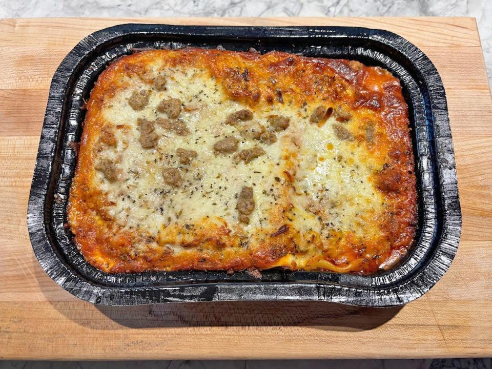 A rectangular black tray of lasagna with bubbling sauce, cheese, and pieces of sausage on top