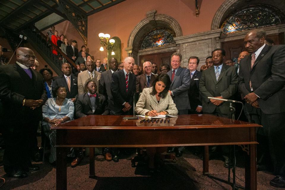 South Carolina Gov. Nikki Haley, surrounded by three former governors, some family members of the slain nine and many legislators, signs the bill to remove the Confederate flag.