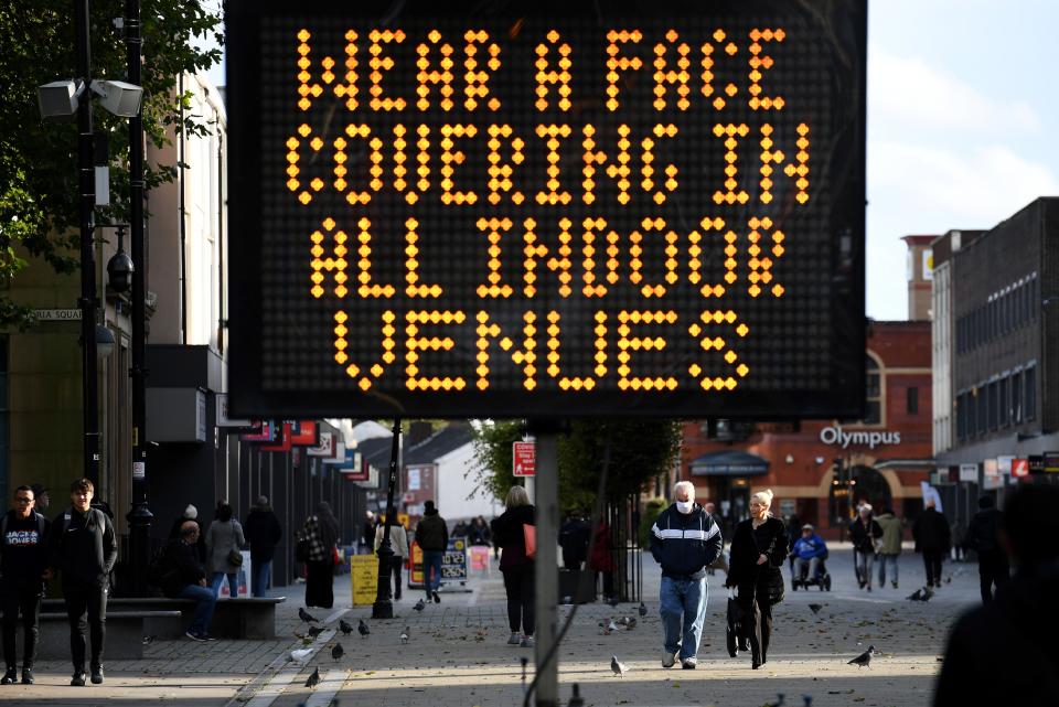 Pedestrians walk past an electronic road sign displaying COVID-19 information advising the use of face coverings for all indoor venues, in Bolton town centre, northwest England on October 7, 2020. - The UK government recently imposed tougher coronavirus restrictions in northwest England, as it voiced fears about rising infection rates among younger people. (Photo by Oli SCARFF / AFP) (Photo by OLI SCARFF/AFP via Getty Images)