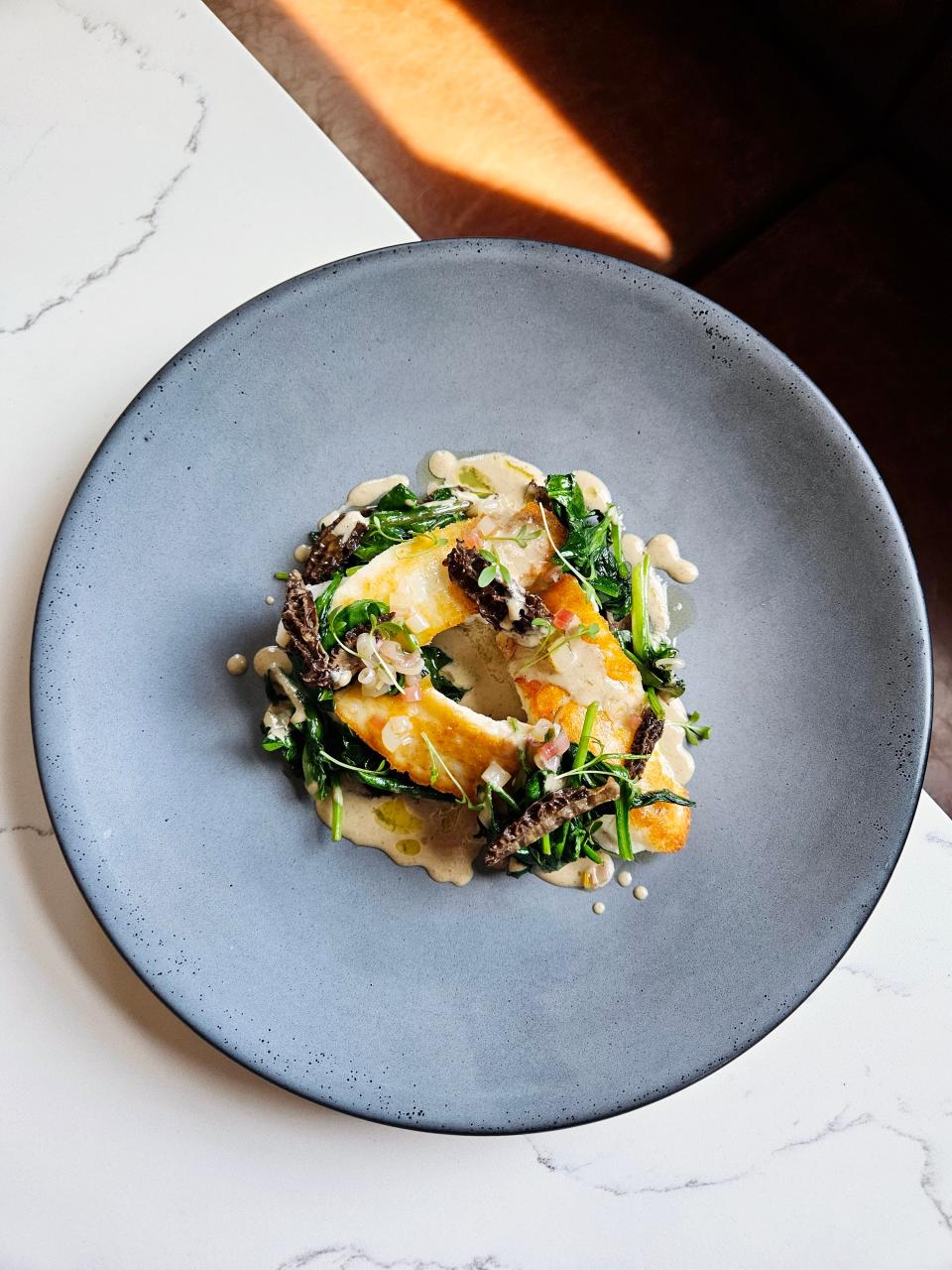 Common Lot's Chef Ehren Ryan 's springtime dish of seared wolf fish with sautéed spinach and ramps, pickled ramps, morels and morel cream sauce.