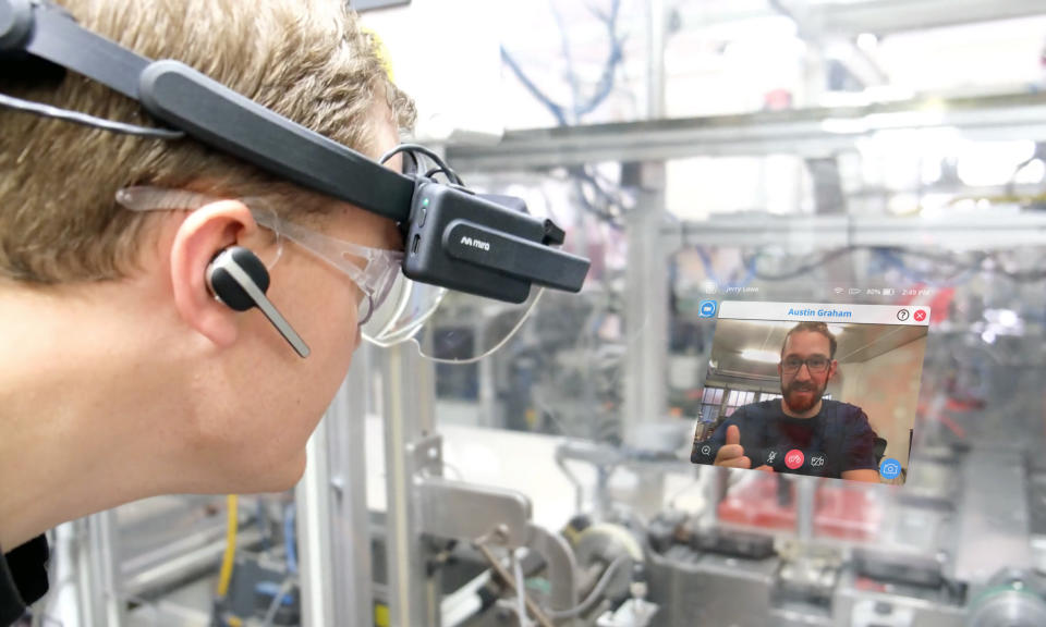 Image of a person (left) wearing a Mira industrial headset, watching a pop-up (augmented) video of a colleague on a video call in a working environment.