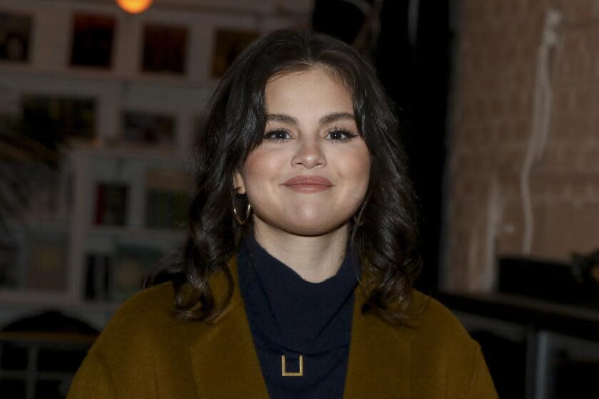 Selena Gomez posing in a brown jacket and black turtleneck