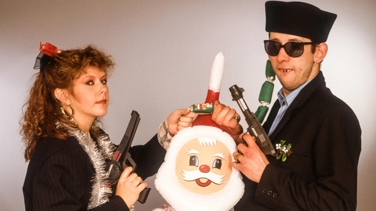  Portrait of British musician Kirsty MacColl (1959 - 2000) and Irish musician Shane MacGowan, the latter of the group the Pogues, as they pose together, each holding a toy gun with one hand and, in the other, a Christmas cracker over an inflatable Santa Claus, 1987. 