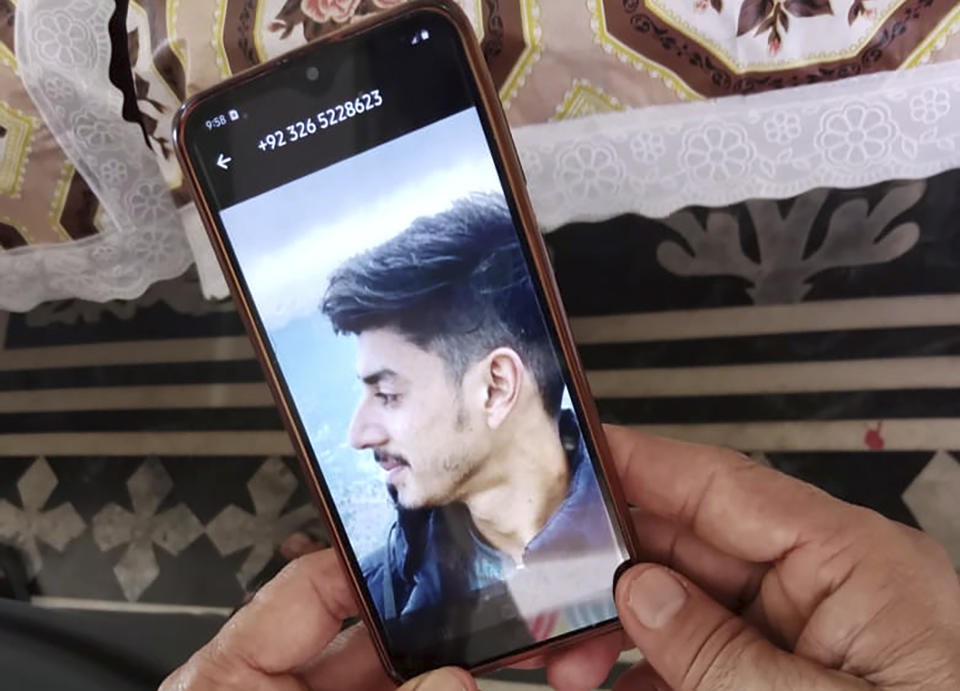 Raja Tariq holds up a picture of his son Raja Awais on his cell phone, who is missing after a shipwreck off the Greek coast, in Bindian village in Kotli, a district of Pakistan's administrator Kashmir, Sunday, June 18, 2023. Pakistani Prime Minister Shehbaz Sharif declared a national day of mourning for citizens who died when the fishing trawler packed with migrants they were in sank off the Greek coast. (AP Photo/Nasir Mehmood)