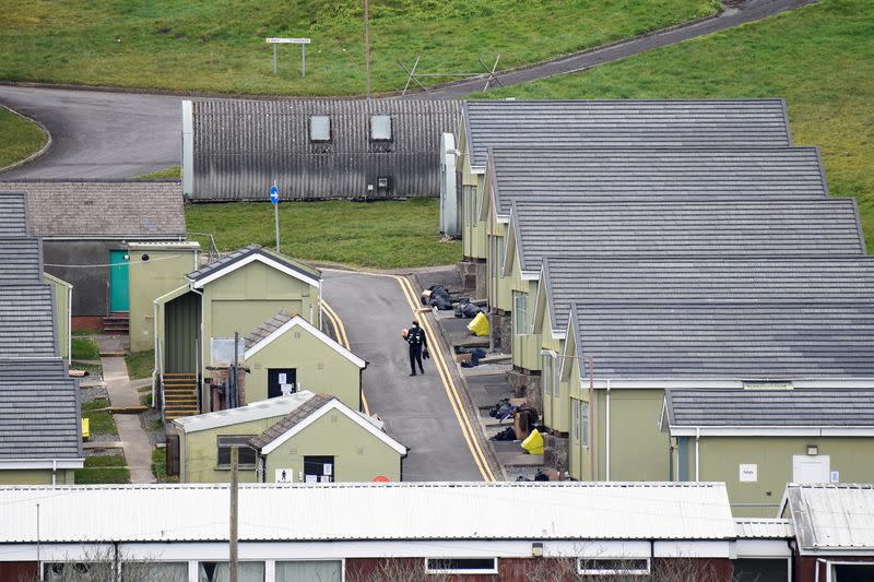 FILE PHOTO: A security guard carries a football and a pair of shoes as Penally camp closes, in Penally, Wales