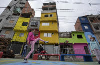 Workers paint the facades of residences in the Paraisopolis favela, as a child plays in the foreground during the community's centennial celebration, in Sao Paulo, Brazil, Thursday, Sept. 16, 2021. One of the largest favela's in Brazil, home to tens of thousands of residents in the country's largest and wealthiest city, Paraisopolis is grappling with crime and a pandemic that have challenged daily life for many who live there, but organizers say its people have built a vibrant community and are launching a 10-day celebration of its achievements. (AP Photo/Andre Penner)