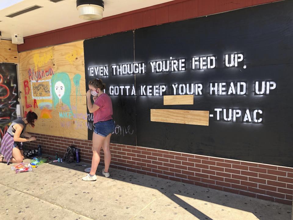 Volunteers paint murals with lyrics from late hip-hop artist Tupac on boarded-up businesses in Kenosha, Wis., on Sunday, Aug. 30, 2020, at an "Uptown Revival." The event was meant to gather donations for Kenosha residents and help businesses hurt by violent protests that sparked fires across the city following the police shooting of Jacob Blake. (AP Photo/ Russell Contreras)