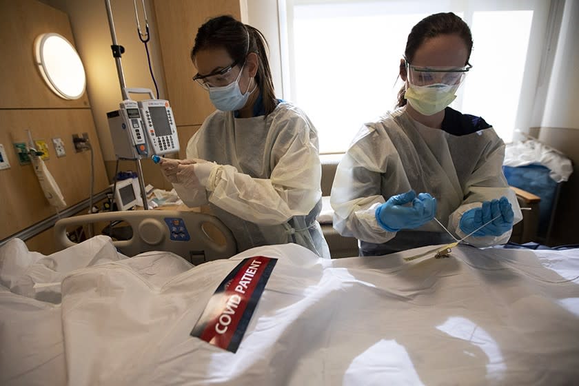 Registered nurses April McFarland, left, and Tiffany Robbins place a body inside a white bag and zip it closed.