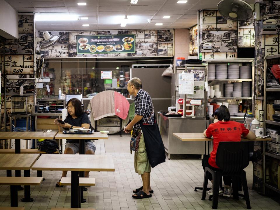 People sitting at tables by a food stall.