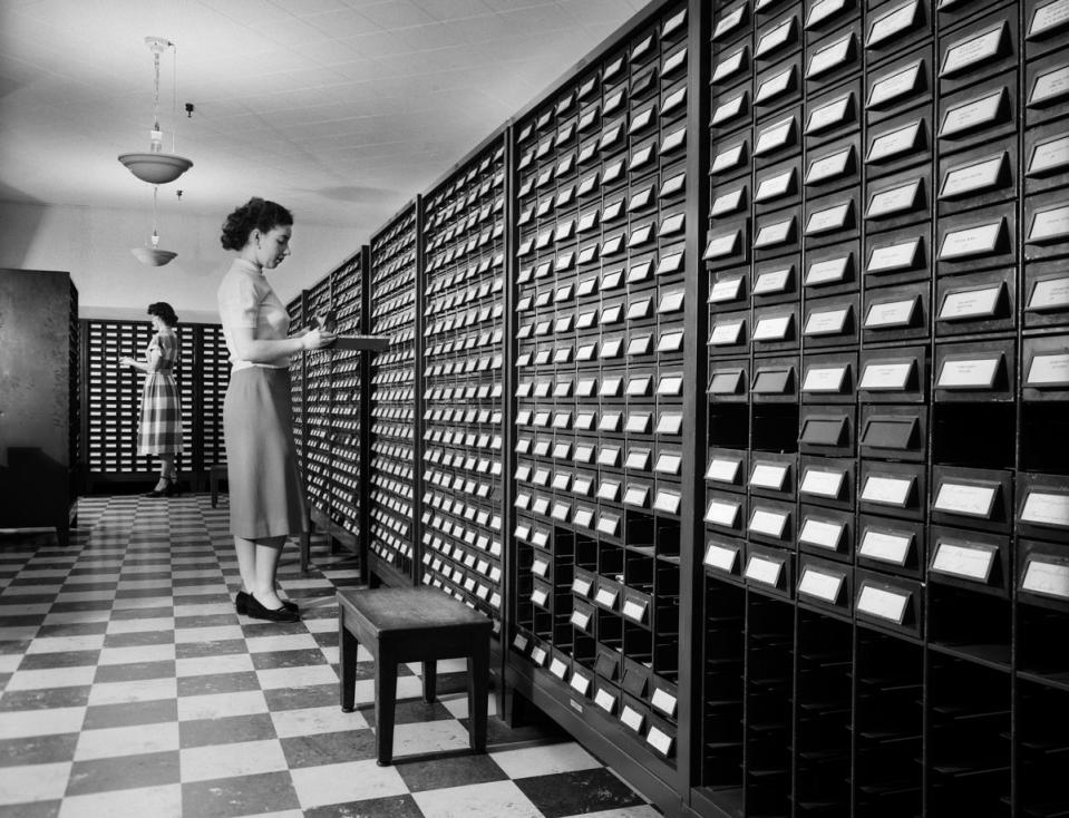 Two women stand beside open drawers of computer punch card filing cabinets. (American Stock/Getty Images)