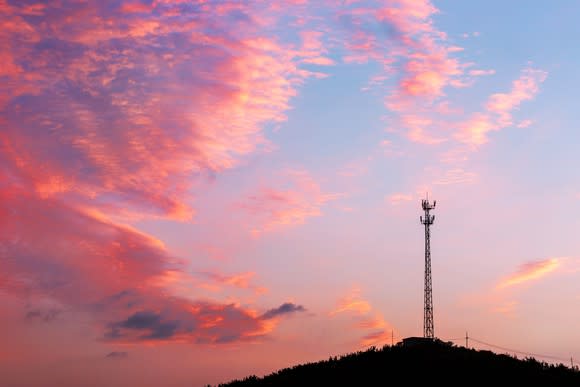 Cell tower on a hill with pink clouds in the sky.