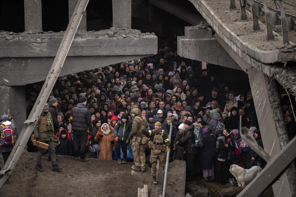 FILE - Ukrainians crowd under a destroyed bridge as they try to flee crossing the Irpin river in the outskirts of Kyiv, Ukraine, Saturday, March 5, 2022. War has been a catastrophe for Ukraine and a crisis for the globe. One year on, thousands of civilians are dead, and countless buildings have been destroyed. Hundreds of thousands of troops have been killed or wounded on each side. Beyond Ukraine’s borders, the invasion shattered European security, redrew nations’ relations with one another and frayed a tightly woven global economy. (AP Photo/Emilio Morenatti, File)