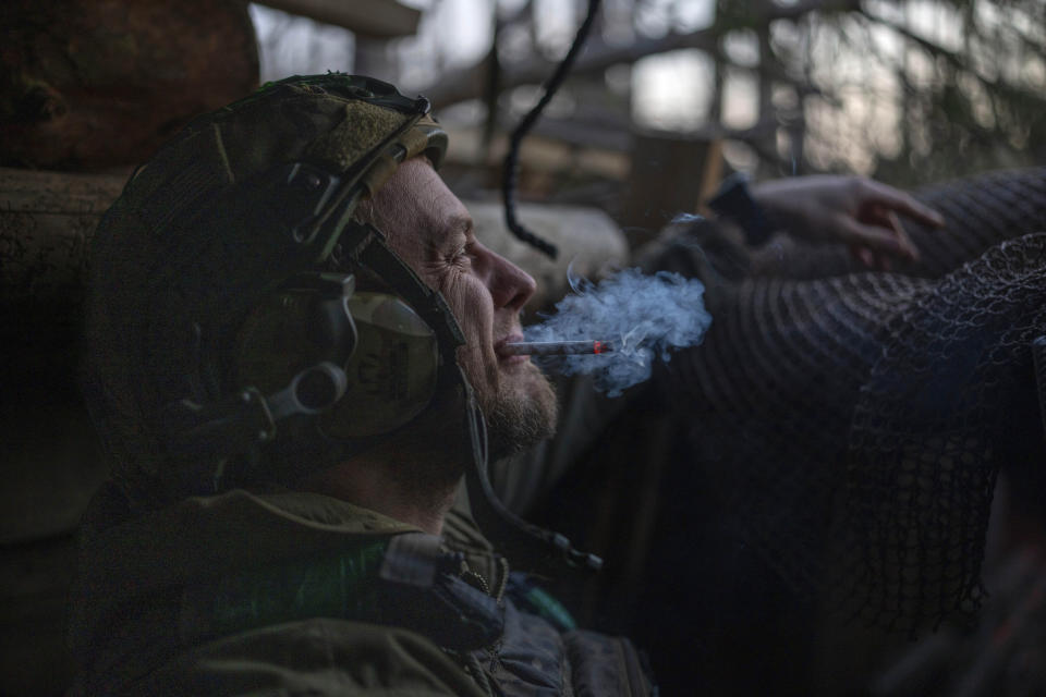 A Ukrainian serviceman from the Azov brigade, known by the call sign Chaos, smokes a cigarette while he waits for a command to fire, in a dugout around one kilometer away from Russian forces on the frontline in Kreminna direction, Donetsk region, Ukraine, Friday, April 12, 2024. (AP Photo/Alex Babenko)