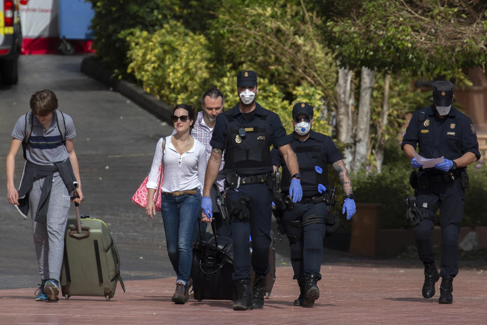 Police officers wearing a face mask walk as guests leave the H10 Costa Adeje Palace hotel in La Caleta, in the Canary Island of Tenerife, Spain, Saturday, Feb. 29, 2020. Some guests have started to leave the locked down hotel after undergoing screening for the new virus that is infecting hundreds worldwide. (AP Photo/Joan Mateu)