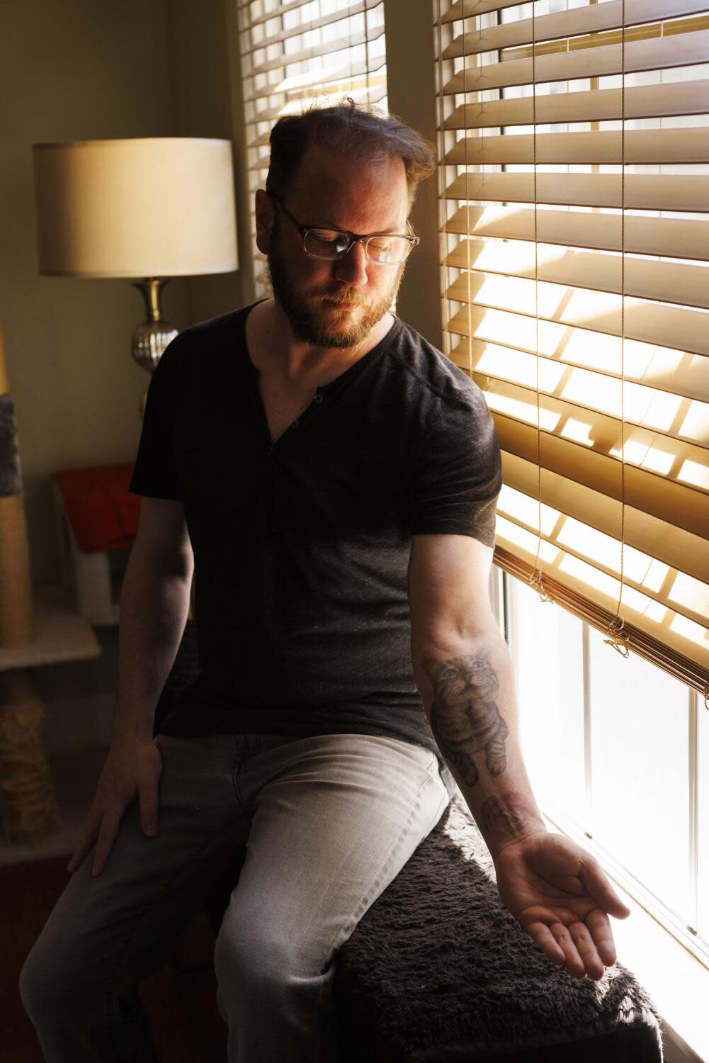 A man sits by a window with half-drawn blinds.