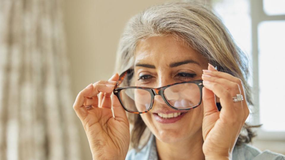 mature woman putting on a pair of glasses as she experiences sharper vision, which is part of the benefits of astaxanthin