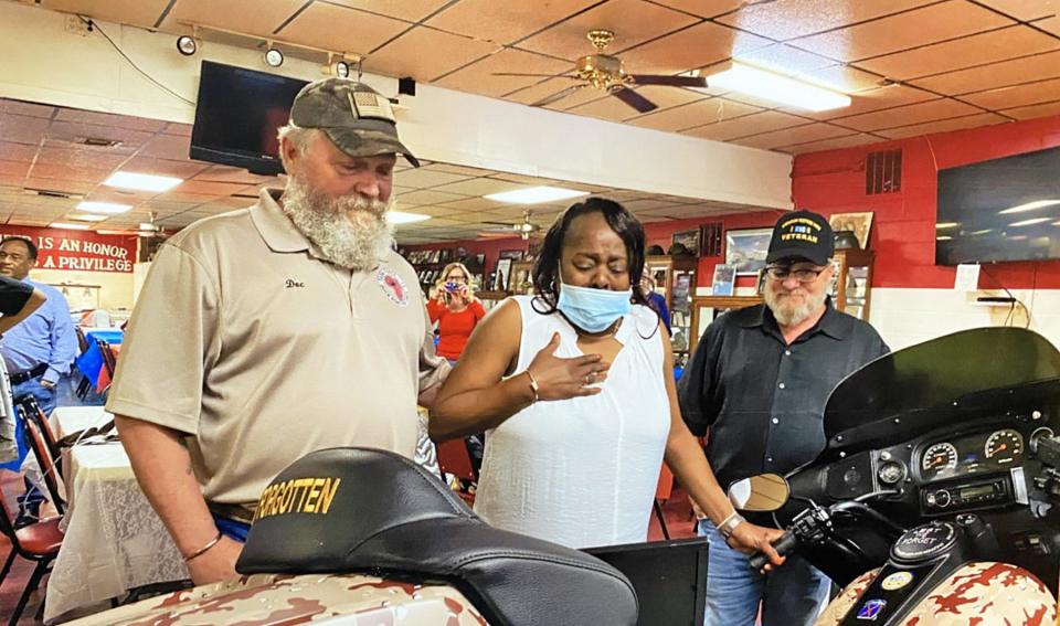 Carmen Houston (center) reacts to seeing her husband's name on the tribute bike created by Ed Ricord (left) while James Wing, another member of the Quick Reaction Task Force 2-14, looks on.