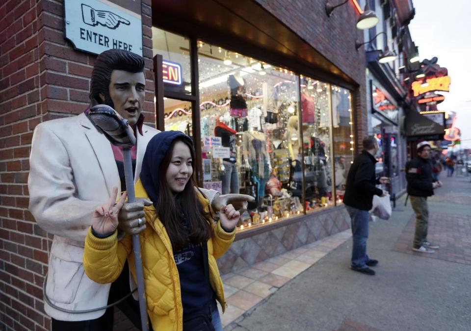 This Jan. 15, 2014 photo shows Kim Young, of Seoul, South Korea, posing for a photo by a statue of Elvis Presley while visiting Broadway in Nashville, Tenn. Broadway is lined with honky tonks, restaurants and souvenir shops.(AP Photo/Mark Humphrey)