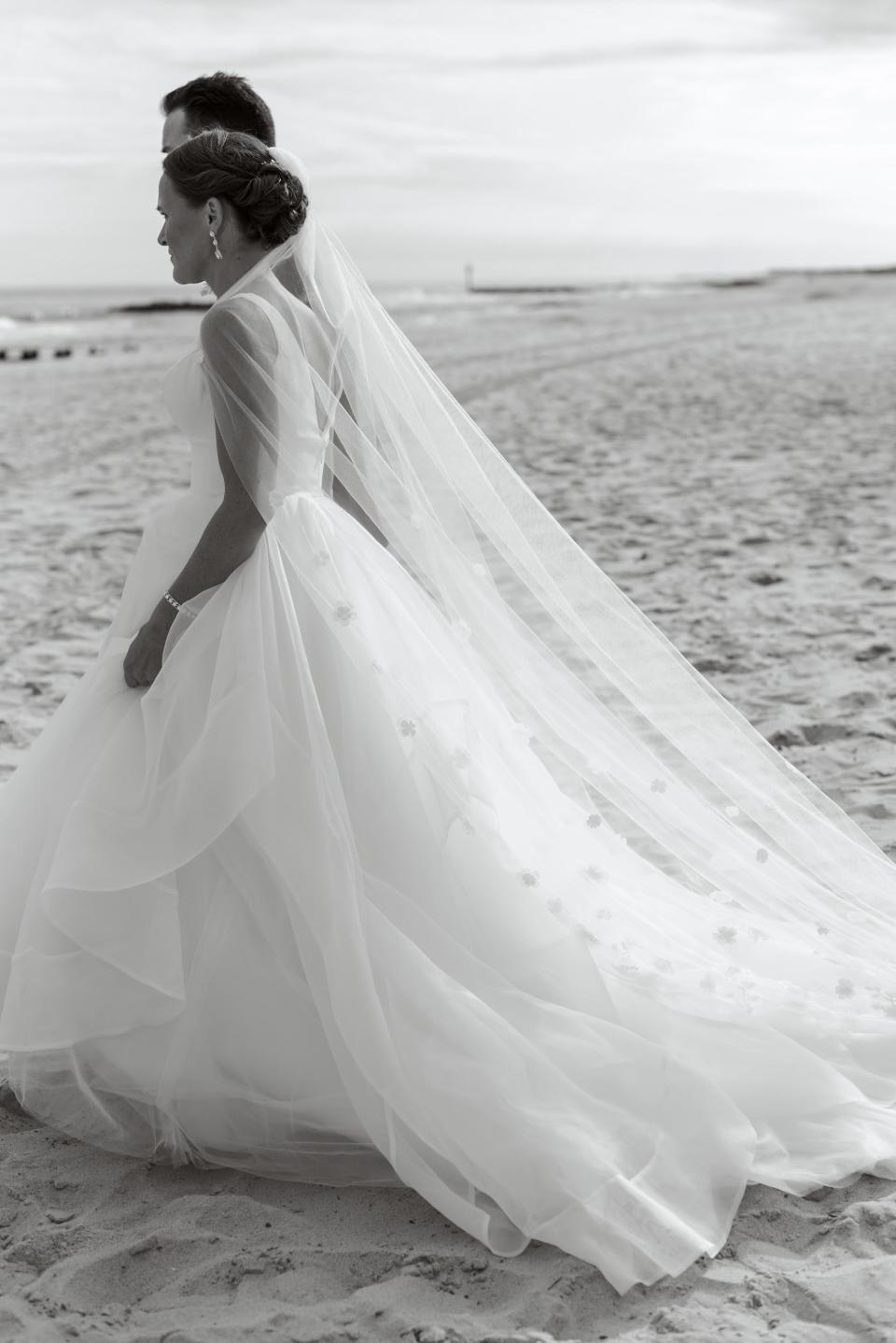 A black and white photo of a bride and groom walking on a beach.