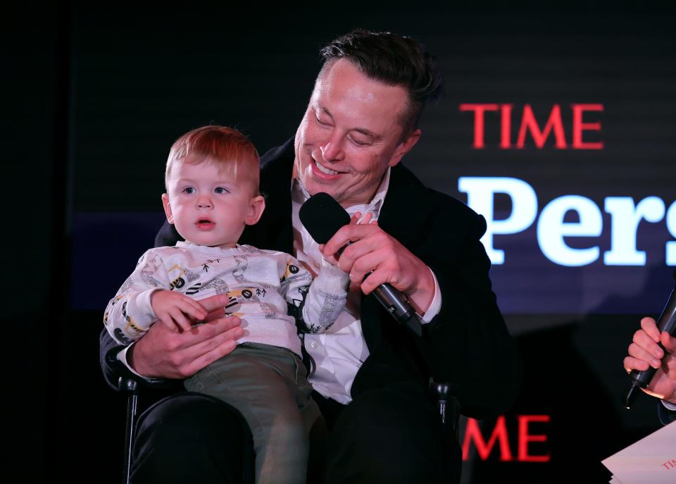Elon Musk holds a microphone while looking at his son, X Æ A-12, who is sitting on his lap