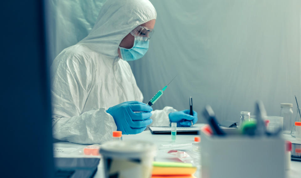 Unrecognizable female scientist with bacteriological protection suit investigating a vaccine in the laboratory