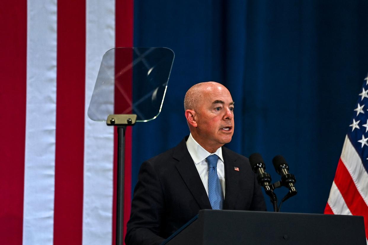 Homeland Security Secretary Alejandro Mayorkas at a podium, flanked by U.S. flags.
