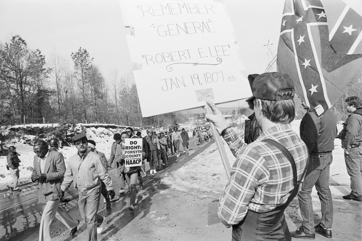 A few racist counterdemonstrators, one of them holding a sign that reads Remember General Robert E. Lee, confront a civil rights march in Cumming, Ga., in 1987.