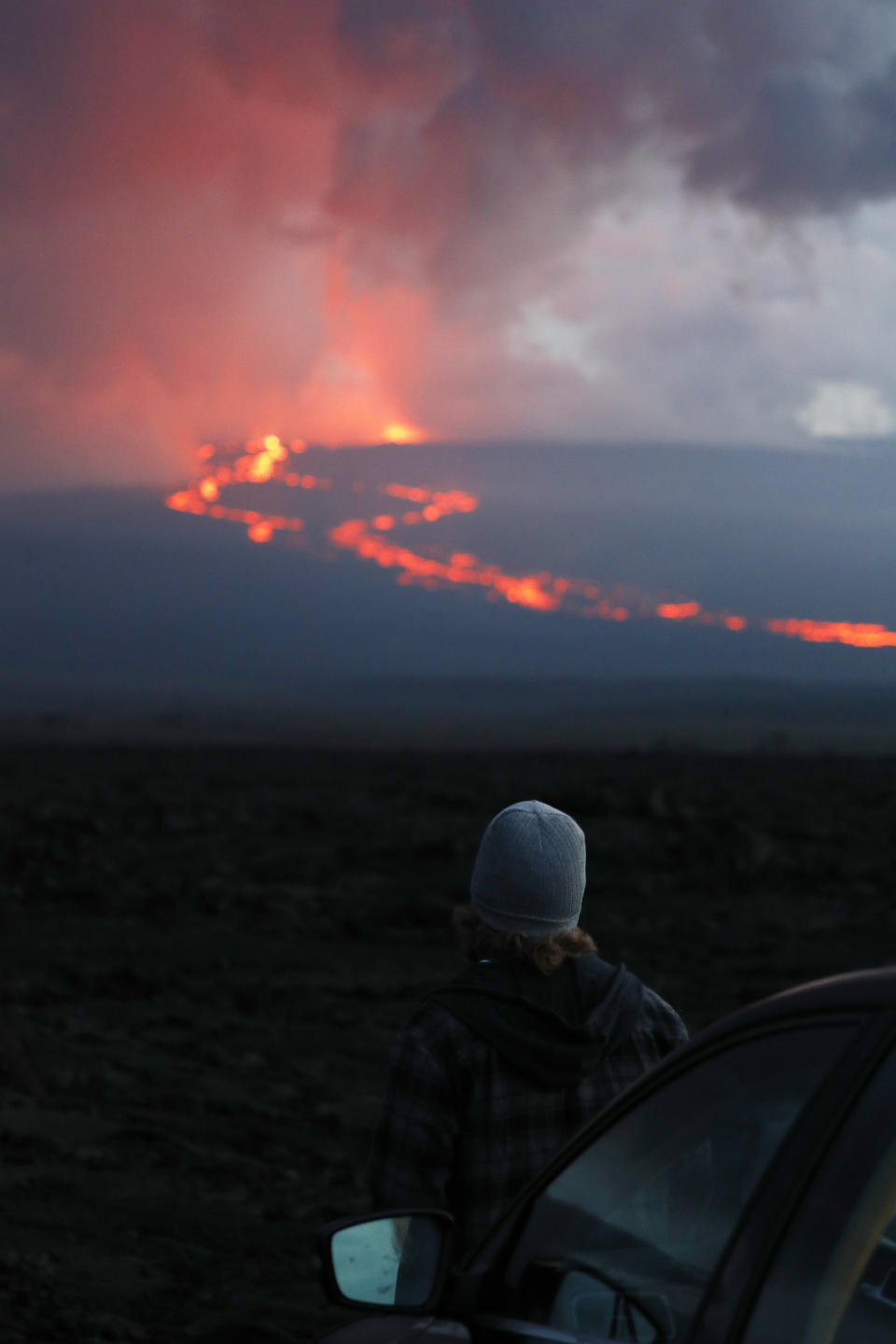 A spectator watches the lava flow down the mountain from the Mauna Loa eruption, Tuesday, Nov. 29, 2022, near Hilo, Hawaii. (AP Photo/Marco Garcia)
