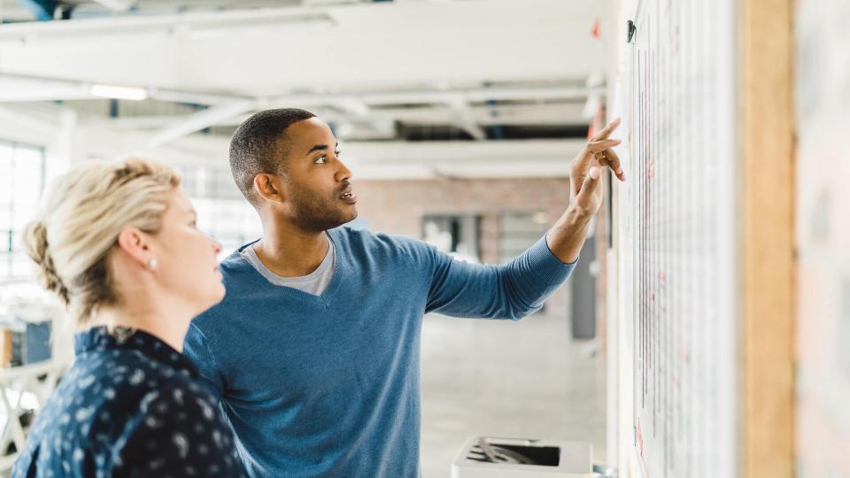 businessman discussing with female colleague over whiteboard.