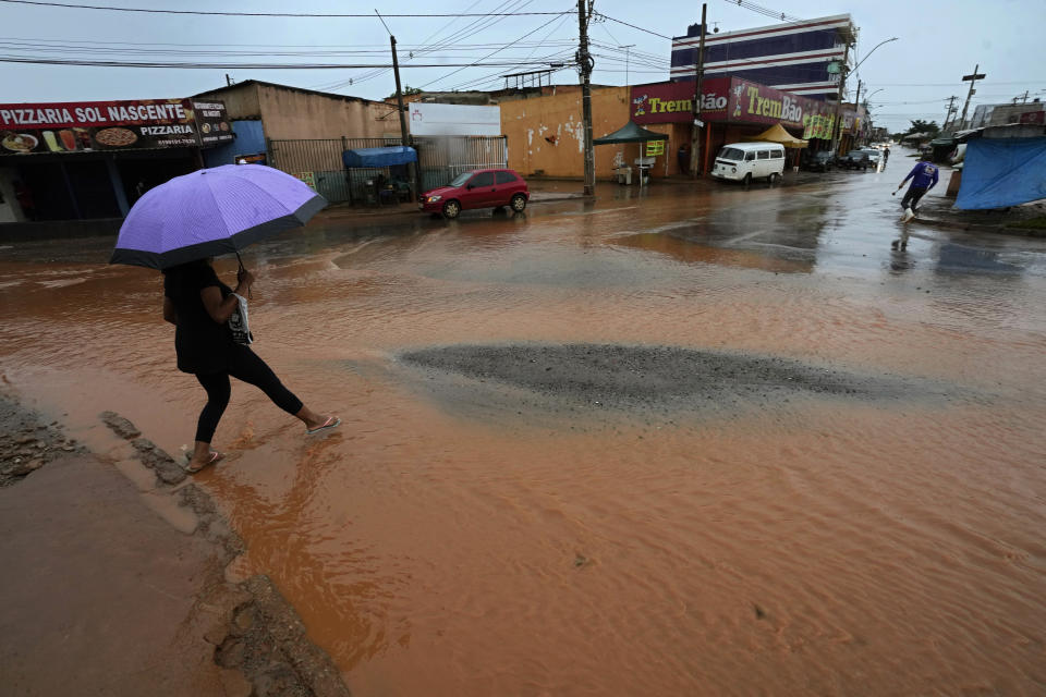 A resident crosses a street flooded by rain in the Sol Nascente favela of Brasilia, Brazil, Tuesday, March 21, 2023. Sol Nascente, which means Rising Sun, suffers poor public transport and has unpaved, impassable roads, which flood frequently during the months of summer rains. (AP Photo/Eraldo Peres)