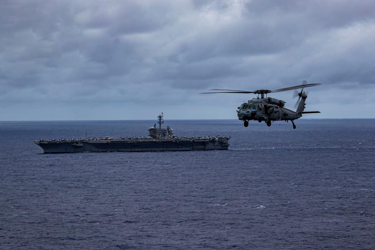 A helicopter flying next to an aircraft carrier at sea.