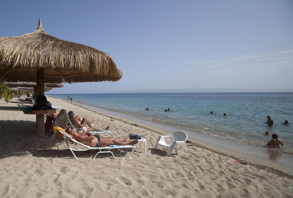 In this June 29, 2013, tourists rest seaside while others wade in the ocean waters at the Club Indigo beach resort in Montrouis, Haiti. While many in Haiti welcome anything that can create jobs, some critics are questioning the government’s priority of trying to attract high-end tourists at a time when the country faces so many other problems, such as high unemployment, a deadly cholera outbreak and lack of housing for people displaced by the earthquake more than three years ago. (AP Photo/Dieu Nalio Chery)