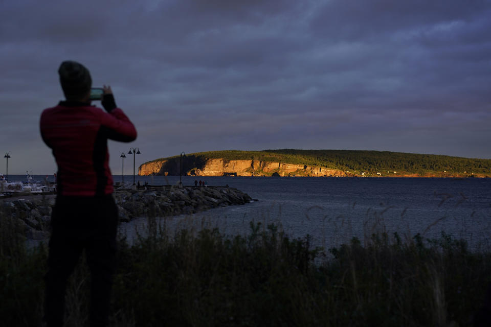 A person takes a photograph of Bonaventure Island across the Gulf of St. Lawrence from Perce, Quebec, Canada, at sunset, Thursday, Sept. 15, 2022. The small island is close to shore and home to over 100,000 gannets in the breeding season, making them the world's second largest northern gannet colony. (AP Photo/Carolyn Kaster)