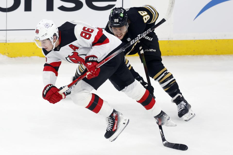 Boston Bruins' David Pastrnak (88) trips New Jersey Devils' Jack Hughes (86) during the first period of an NHL hockey game Saturday, Dec. 30, 2023, in Boston. (AP Photo/Michael Dwyer)