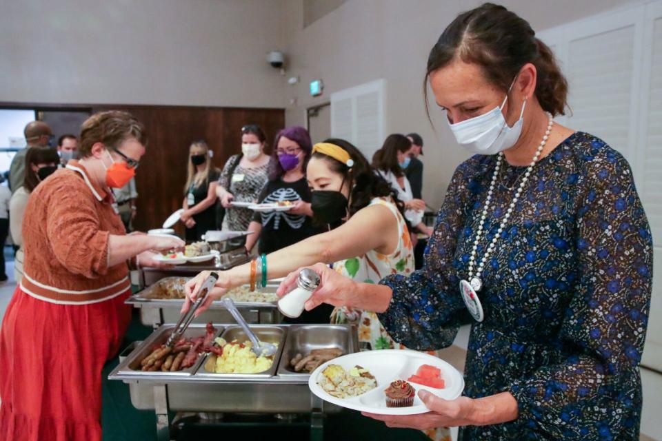 A woman sprinkling salt over her breakfast at the end of a buffet line.