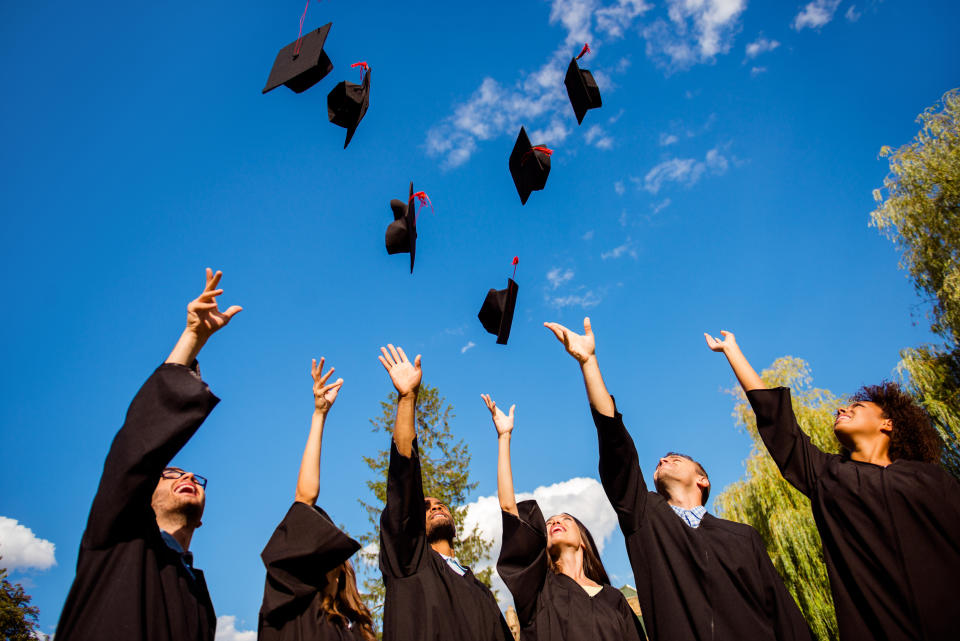 Congratulations! Low angle view of happy group of six young cheerful multi ethnic graduates in black gowns are throwing up their hats in the air and celebrating, laughing, enjoying