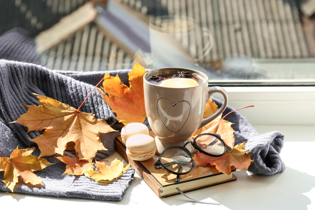 Cup of aromatic tea with book, warm sweater and autumn leaves on windowsill