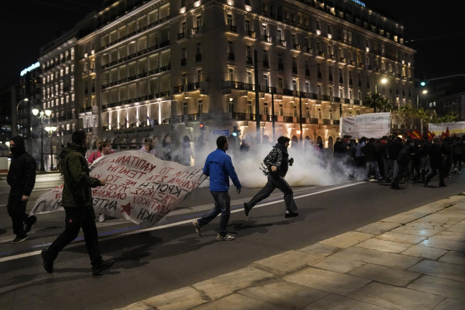 Protesters try to avoid tear gas thrown by riot police in front of the Greek Parliament, in Athens, on Wednesday, March 1, 2023. Several hundred left-wing protesters marched through the city center to protest the deaths of dozens of people late Tuesday, in Greece's worst recorded rail accident. (AP Photo/Petros Giannakouris)