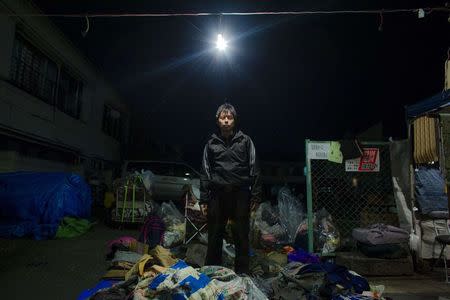 Trader Kazumoto Miyaoka poses in the pile of secondhand clothes and rags that he sells at Boroichi flea market in Tokyo December 15, 2014. REUTERS/Thomas Peter