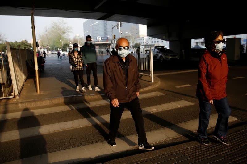 People wearing protective face masks walk across a street in Beijing, as the spread of the novel coronavirus disease (COVID-19) continues in the country