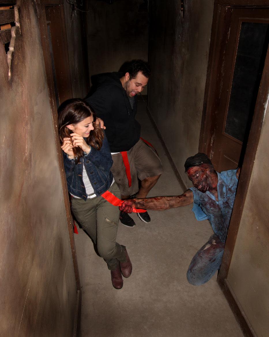 This August 2013 image provided by Shocktoberfest shows an actor portraying a zombie grabs a flag from the belt of someone walking through the Prison of the Dead Escape, part of the Shocktoberfest attraction in Reading, Pa. Halloween-themed attractions are becoming more interactive, with guests no longer merely passive observers walking through a haunted house, but often engaging in a game or challenge as part of the experience. (AP Photo/Shocktoberfest)