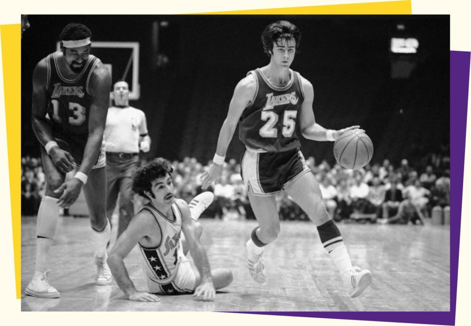 A black-and-white photo of three basketball players. One dribbles a ball around a player on the floor.