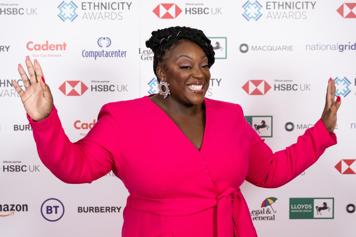 Judi Love gestures with her arms and smiles, wearing a bright pink long-sleeved dress as she attends The Ethnicity Awards 2023 at London Marriot Hotel