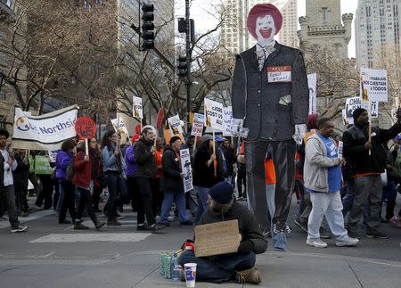 Protesters carrying a cutout of McDonald's character Ronald McDonald march past a homeless person during a demonstration calling for a $15-an-hour nationwide minimum wage in downtown Chicago, Illinois, United States, April 14, 2016. REUTERS/Jim Young