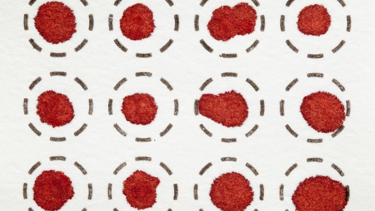  Three rows of four dried blood spot tests on white fiber filter.  The top and bottom rows are slightly cut off by the image dimensions. In each test, a red spot of blood can be seen in inside a circle drawn using dashed black lines. 