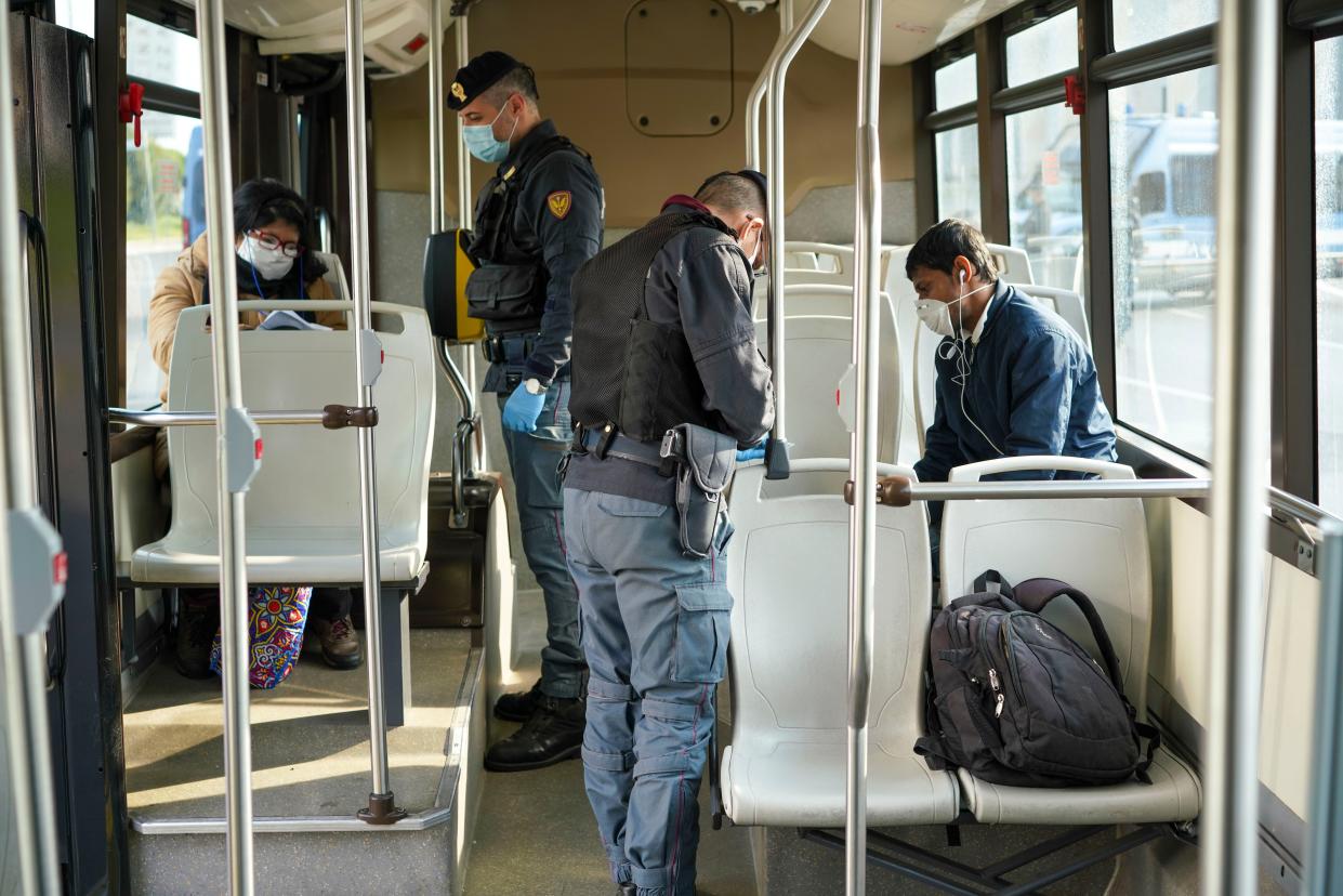 Police officers check documents of passengers on a public bus at a road block, in Rome, Italy on Monday, April 13, 2020.