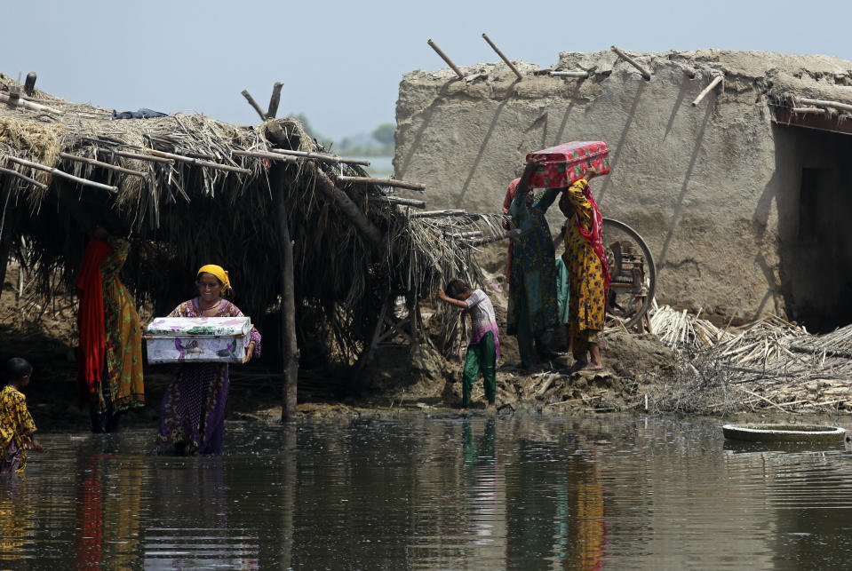 Women carry belongings salvaged from their flooded home after monsoon rains, in the Qambar Shahdadkot district of Sindh Province, of Pakistan, Tuesday, Sept. 6, 2022. More than 1,300 people have been killed and millions have lost their homes in flooding caused by unusually heavy monsoon rains in Pakistan this year that many experts have blamed on climate change. (AP Photo/Fareed Khan)