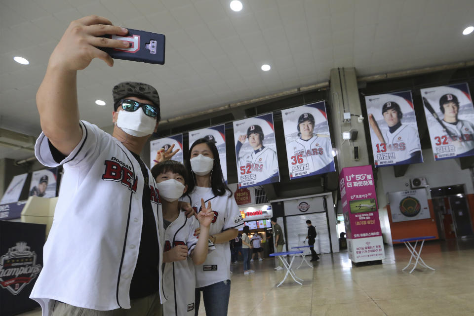 Fans wearing face masks to help protect against the spread of the new coronavirus take a selfie as they arrive to watch the KBO league game between Doosan Bears and LG Twins in Seoul, South Korea, Sunday, July 27, 2020. South Korean Baseball Organization (KBO) on Sunday started admitting fans to the games but only at 10% capacity for each venue.(AP Photo/Ahn Young-joon)