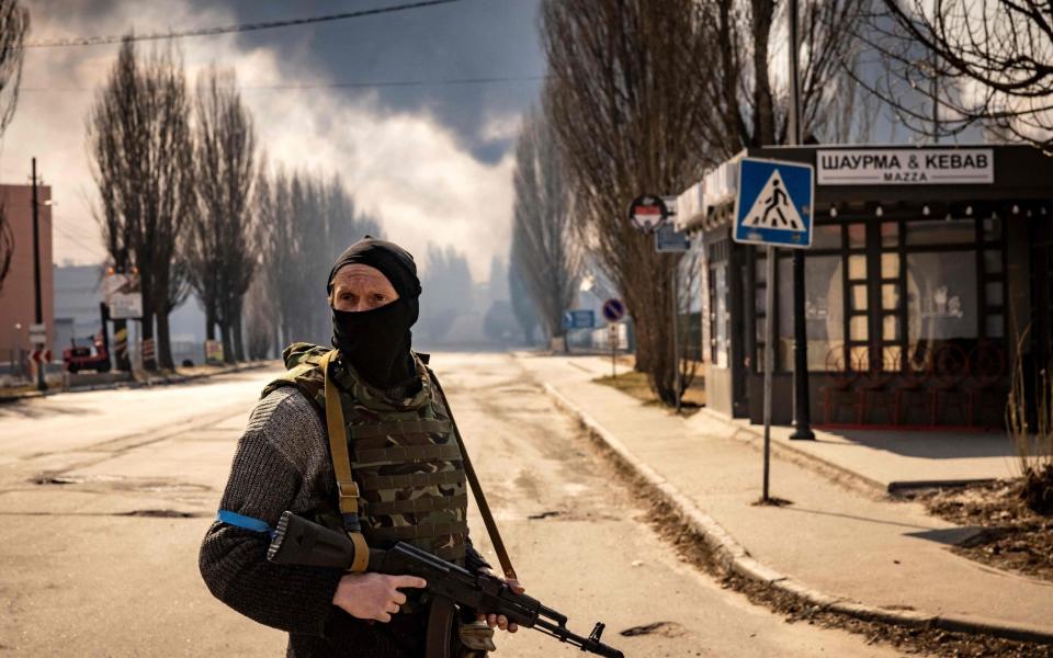 A Ukrainian serviceman stands guard near a burning warehouse in Mariupol. People in the city have described huge destruction and residents resorting to desperate measures to survive - Fadel Senna/AFP via Getty Images